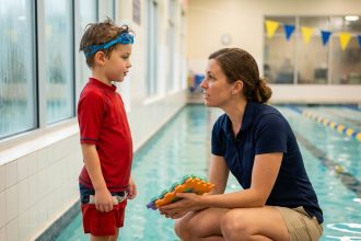 Jeune garçon en maillot de bain au bord d'une piscine intérieure en séance avec une orthophoniste
